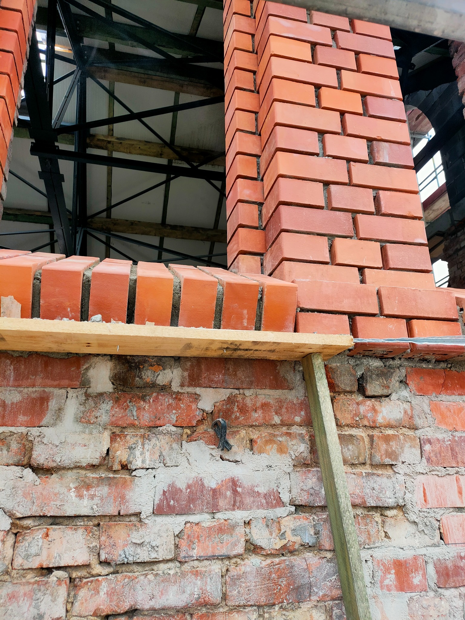 Fragment muru z czerwonej cegły podczas budowy okna, widoczne rusztowanie i drewniane podpory.
