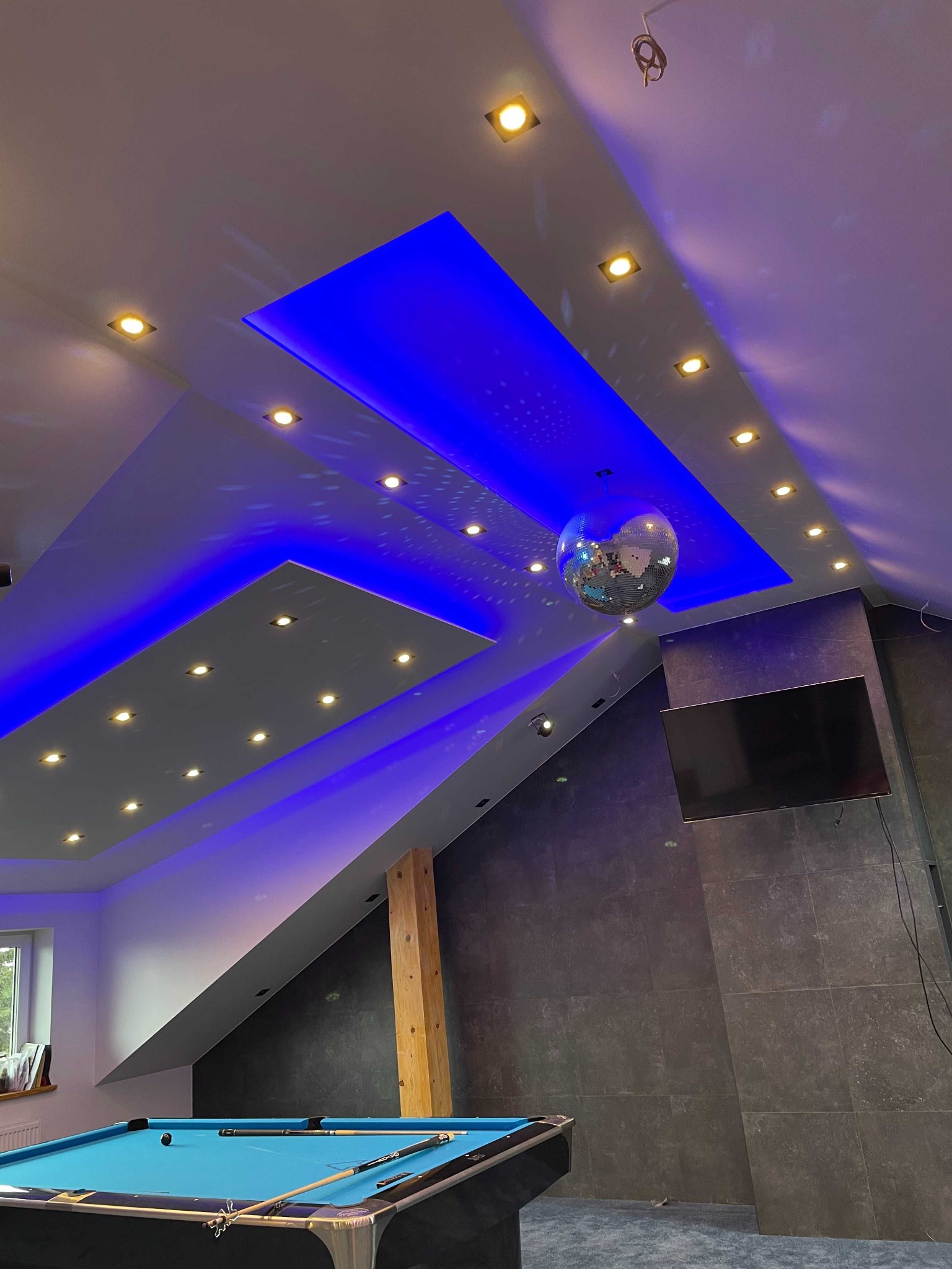Pokój z niebieskim stołem bilardowym, disco kulą i podświetlanym sufitem z oświetleniem punktowym, wykończony glazurą.
