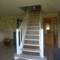 Lucas bau - Białe, drewniane schody z zaokrąglonym podestem początkowym w trakcie montażu w domu w Stargardzie, widoczny piec typu koza i niedokończone ściany.