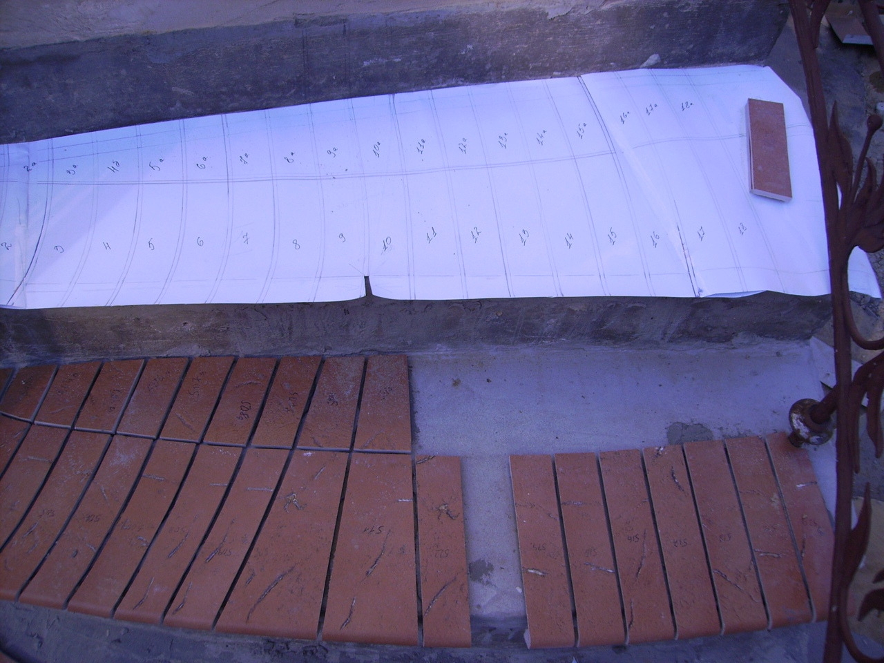 Przygotowanie do ułożenia płytek: szablon z naniesionymi numerami i docięte płytki z oznaczeniami, leżące na podłożu.