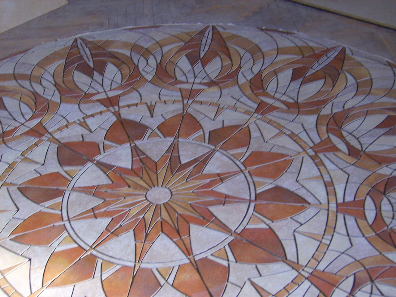 Dekoracyjna mozaika podłogowa z geometrycznym wzorem w odcieniach brązu i beżu, ułożona z drobnych płytek.