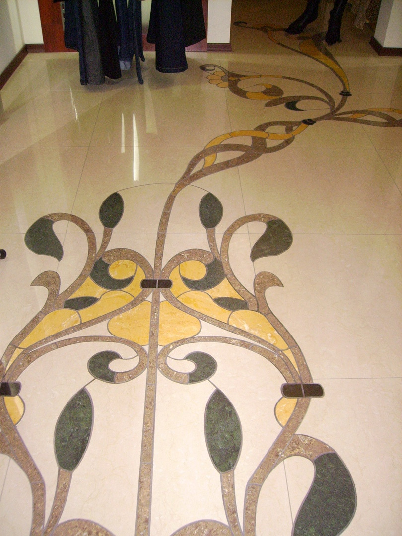 Beżowa podłoga z płytek z inkrustowanym wzorem roślinnym w odcieniach zieleni, brązu i żółci.