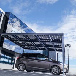 Nowoczesny budynek z panelami słonecznymi na fasadzie i zadaszenie solarne dla samochodu, brązowy minivan zaparkowany pod wiatą