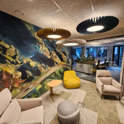 Nowoczesne biuro z abstrakcyjnym malowidłem na ścianie, designerskimi lampami, beżowymi fotelami i żółtym krzesłem.