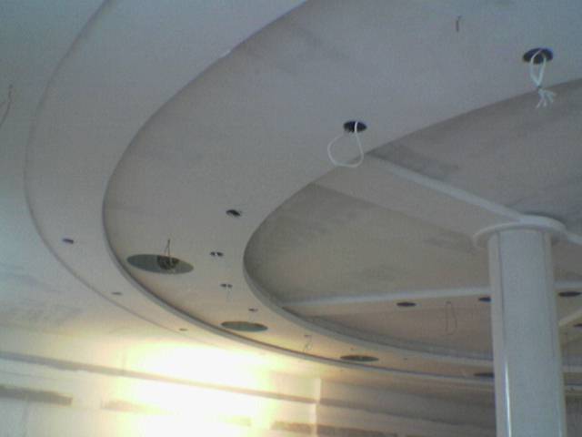 Niedokończony sufit podwieszany z elementami łukowymi i przygotowanymi otworami na oświetlenie, widoczny filar konstrukcyjny.