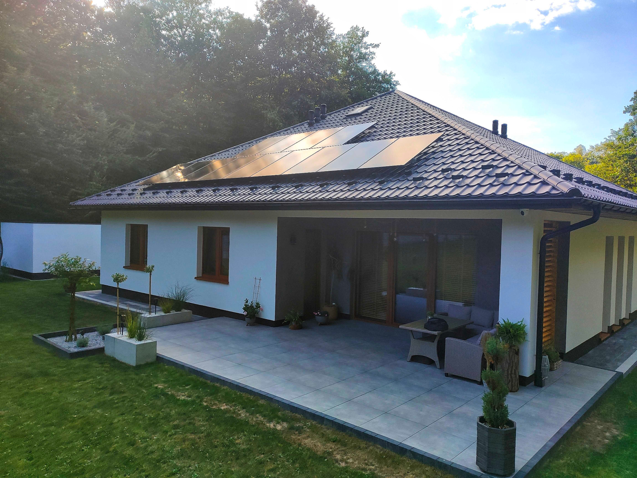 Nowoczesny dom jednorodzinny z panelami słonecznymi na dachu z dachówki ceramicznej, widok z ogrodu w słoneczny dzień.