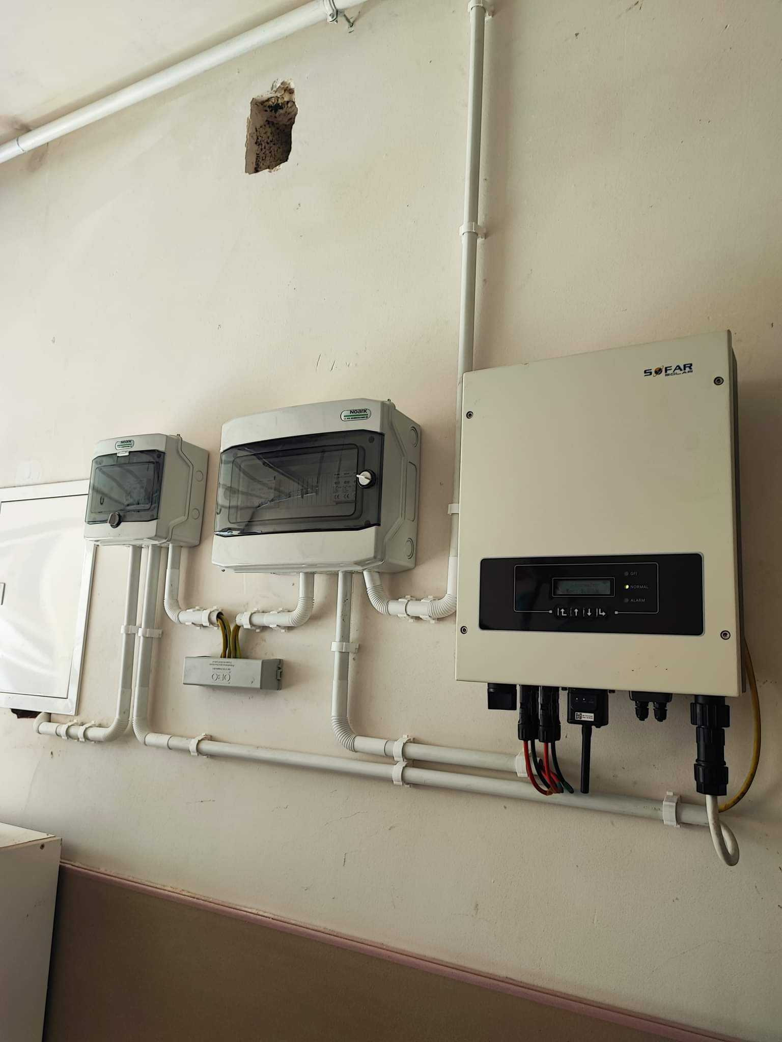 Instalacja elektryczna z inwerterem Sofar Solar i dwoma zabezpieczeniami w obudowach na kremowej ścianie z widoczną dziurą, rurki PCV prowadzone po ścianie.
