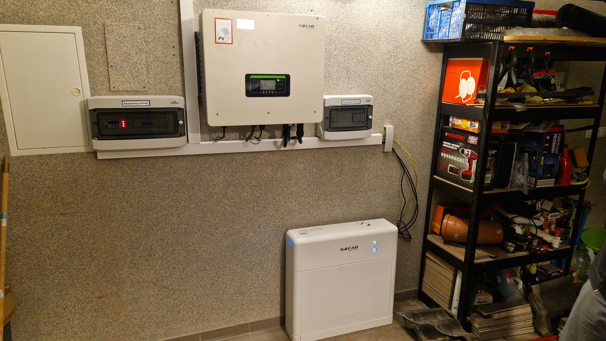 Instalacja z inwerterem SOFAR, rozdzielnicami PV-AC i PV-DC oraz magazynem energii, zamontowana na ścianie z widoczną półką z narzędziami i akcesoriami.