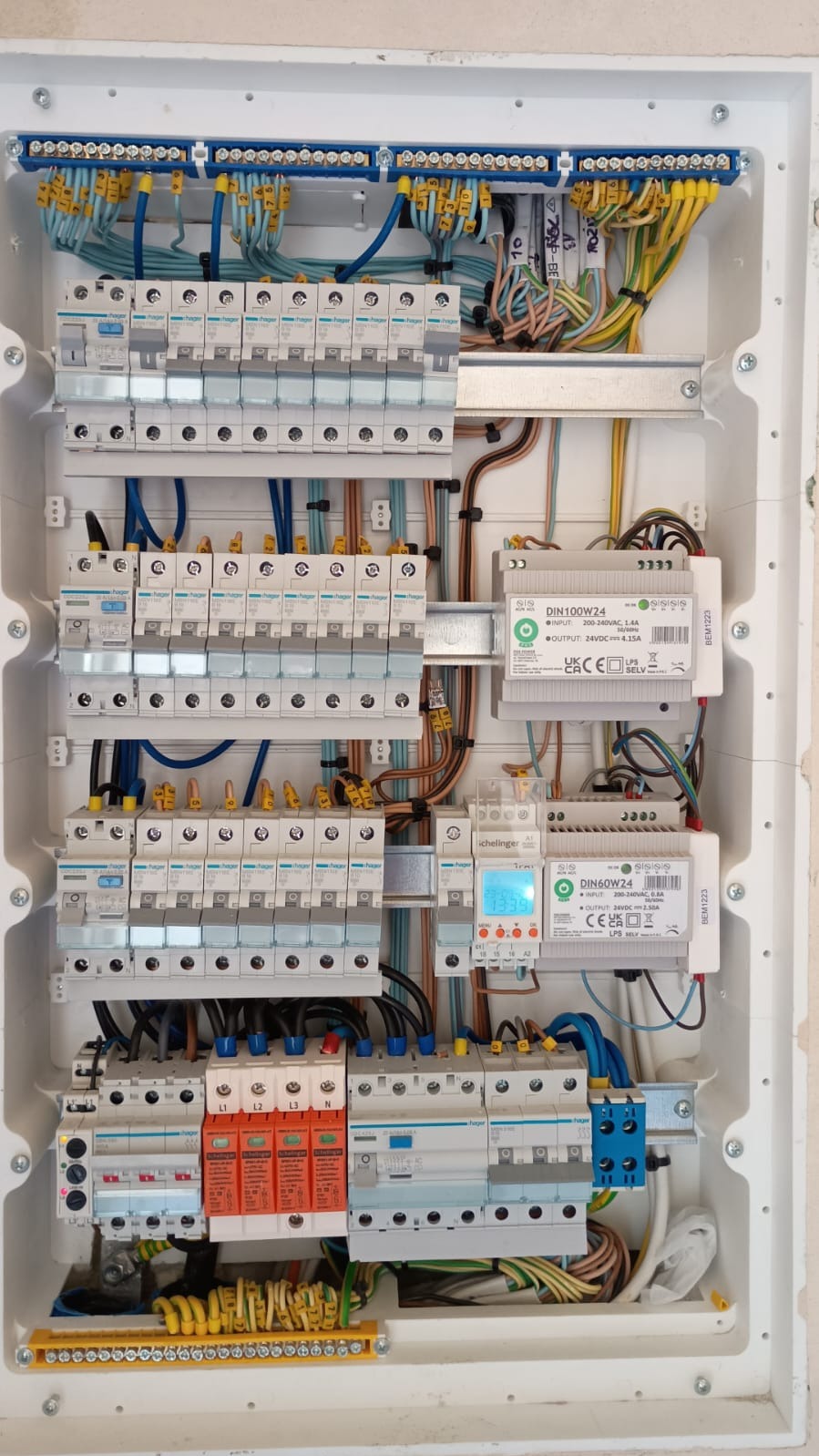 Rozdzielnica elektryczna z licznymi bezpiecznikami, przewodami oznaczonymi numerami i modułami z wyświetlaczami, zamontowana w białej obudowie.