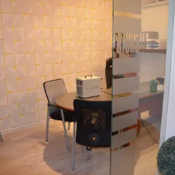 Urządzenie AirClean na okrągłym stole w biurze z geometryczną ścianą, prawdopodobnie używane do dezynfekcji lub oczyszczania powietrza.