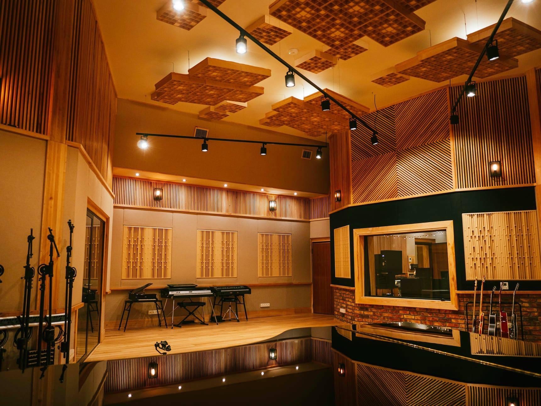 Profesjonalnie przygotowane akustyczne pomieszczenie z drewnianymi panelami, oświetleniem punktowym i instrumentami muzycznymi, w tym keyboardami i gitarami.