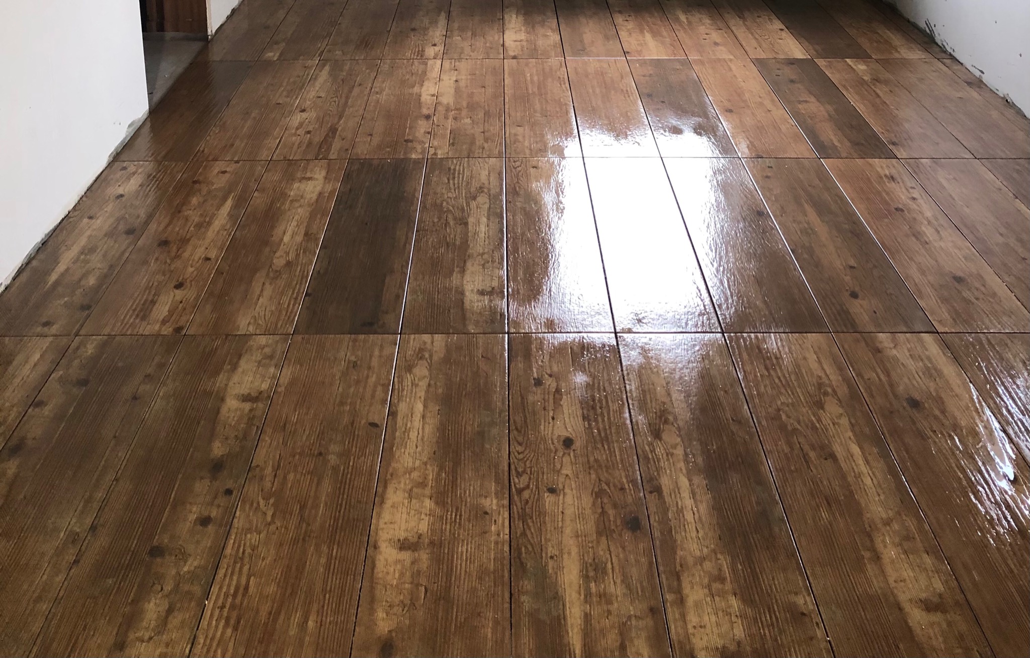 Świeżo położona, błyszcząca podłoga z płytek imitujących drewno, z widocznymi fugami i odbiciami światła, na tle białej ściany w trakcie wykończenia.