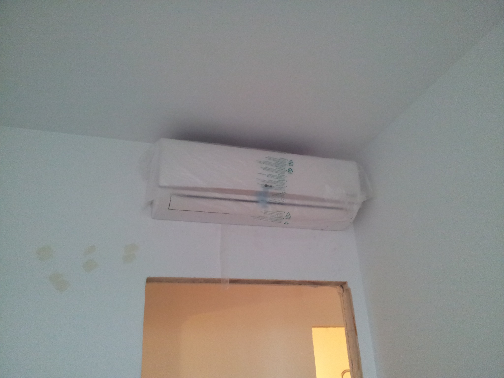 Nowo zamontowany klimatyzator LG w folii ochronnej, widoczne ślady po szpachlowaniu na ścianie, przygotowanie do malowania.