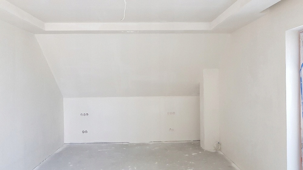 Poddasze po remoncie: białe ściany, wykończona zabudowa sufitu, gładkie powierzchnie gotowe do dalszych prac wykończeniowych, widoczne gniazdka elektryczne.