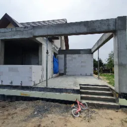 Surowa konstrukcja tarasu z betonu i bloczków, widoczne zbrojenia i stopnie, na ziemi leży różowy rowerek biegowy.