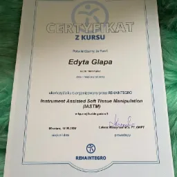 Certyfikat ukończenia kursu Instrument Assisted Soft Tissue Manipulation (IASTM) przez Edytę Glapę, wydany przez REHAINTEGRO z podpisem Łukasza Muszyńskiego, na tle zielonego futerka.