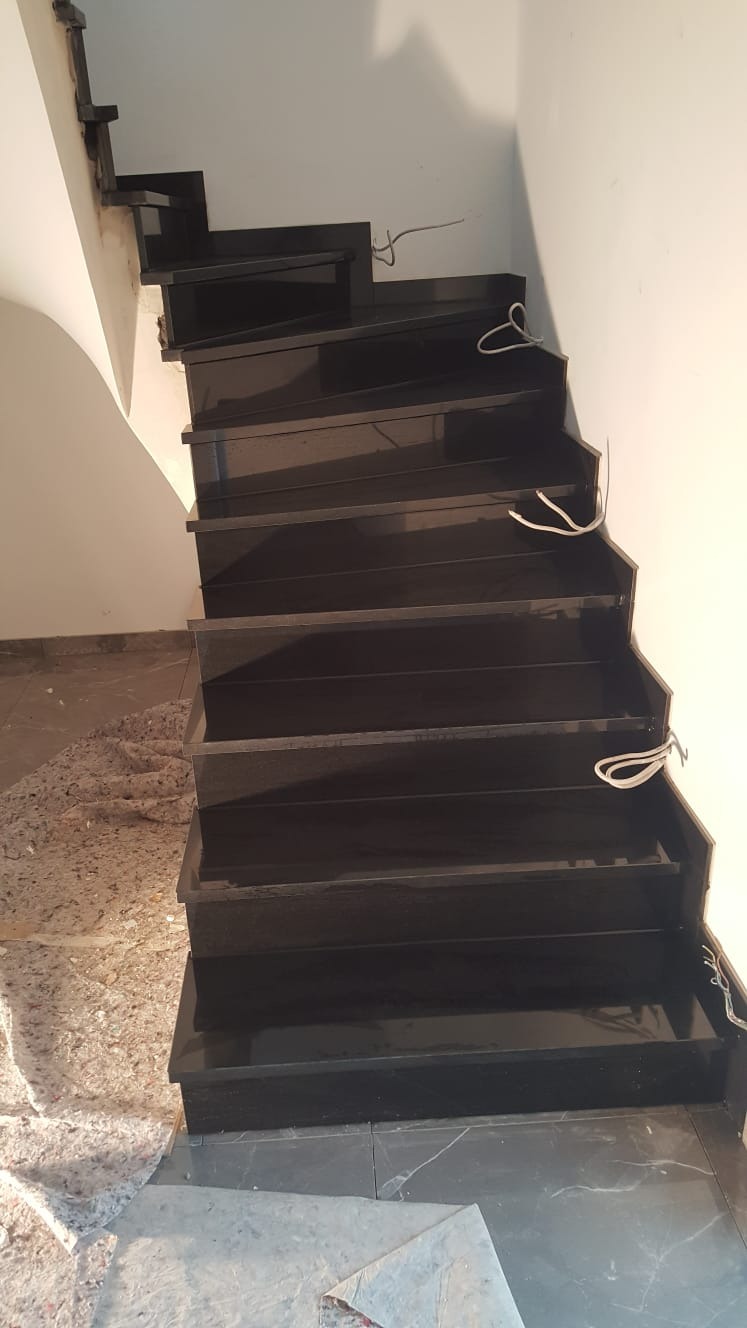 Schody wyłożone czarnym kamieniem, widoczne kable instalacyjne, podłoga częściowo zabezpieczona folią ochronną.