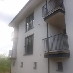 Nowoczesny budynek wielorodzinny z balkonami zabezpieczonymi metalowymi barierkami w kolorze grafitowym, widok z dołu.