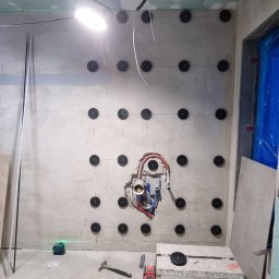 Geo Glazura profesjonalne glazurnictwo - Ściana z zamocowanymi kołkami, widoczne instalacje wodne i elektryczne, narzędzia pracy, poziomica laserowa. Przygotowanie do prac wykończeniowych w pomieszczeniu.
