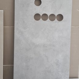 Geo Glazura profesjonalne glazurnictwo - Płyta gresowa z wyciętymi otworami na instalacje, ułożona pionowo na kartonie. Widoczne otwory: jeden u góry, cztery w rzędzie pośrodku i jeden na dole.