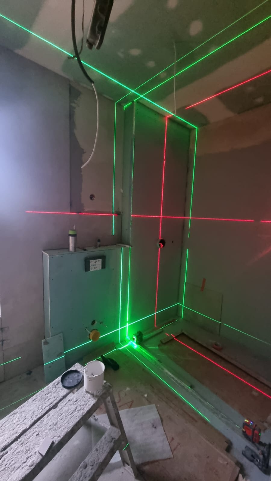 Łazienka w trakcie prac wykończeniowych, widoczne zielone i czerwone linie lasera wyznaczające poziom, ściany przygotowane pod płytki, stelaż podtynkowy.
