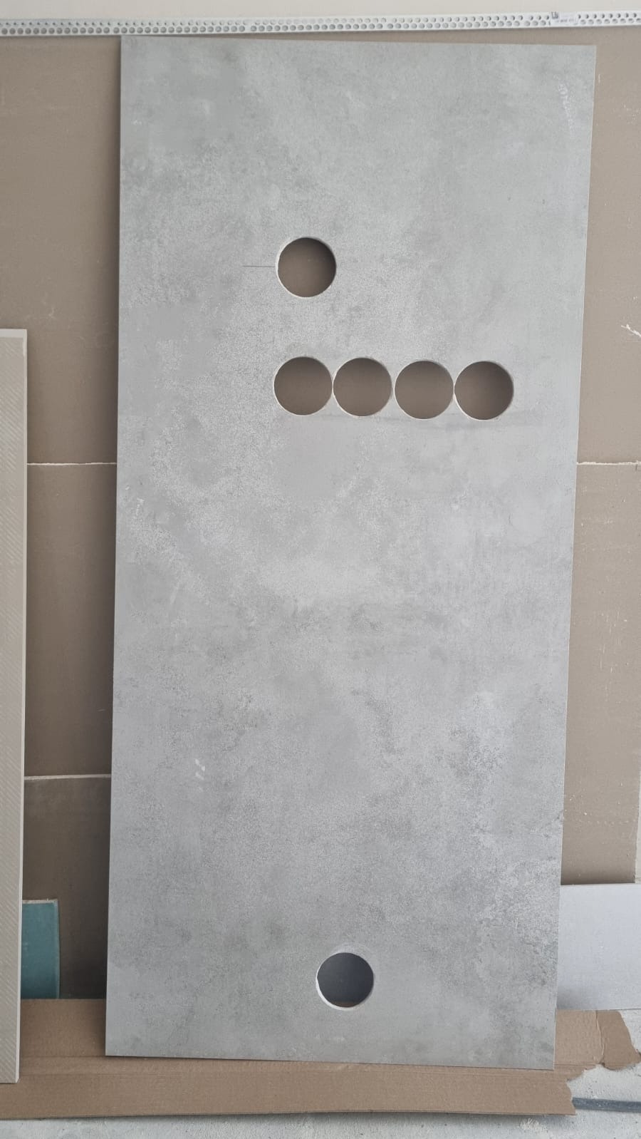 Płyta gresowa z wyciętymi otworami na instalacje, ułożona pionowo na kartonie. Widoczne otwory: jeden u góry, cztery w rzędzie pośrodku i jeden na dole.