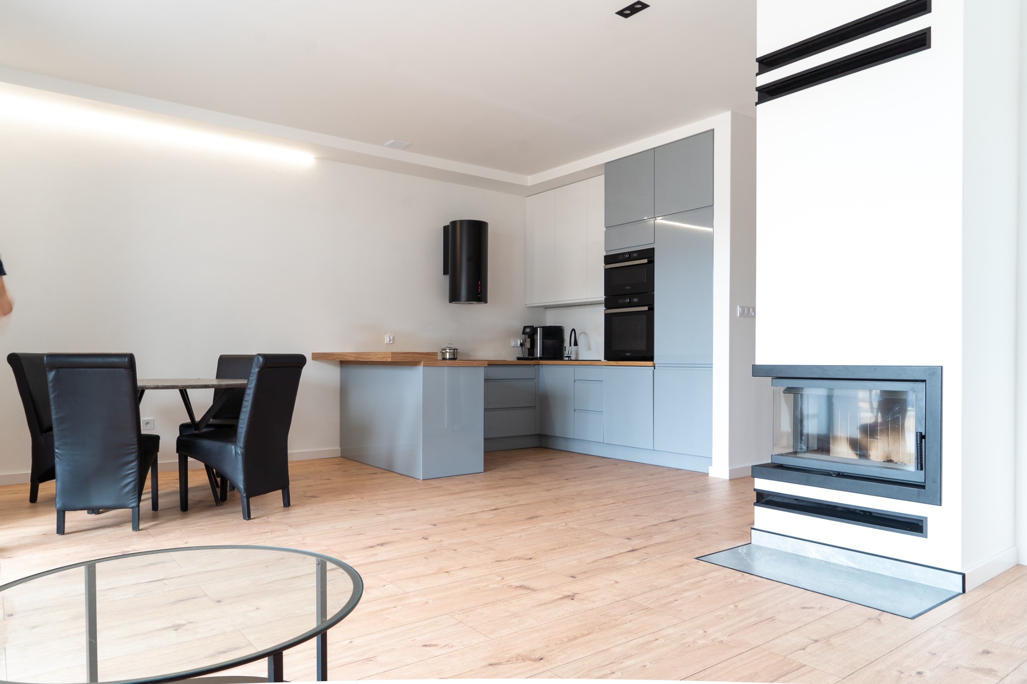 Nowoczesne wnętrze mieszkania w Szczecinku z otwartą kuchnią w odcieniach szarości i bieli, drewnianą podłogą i kominkiem.