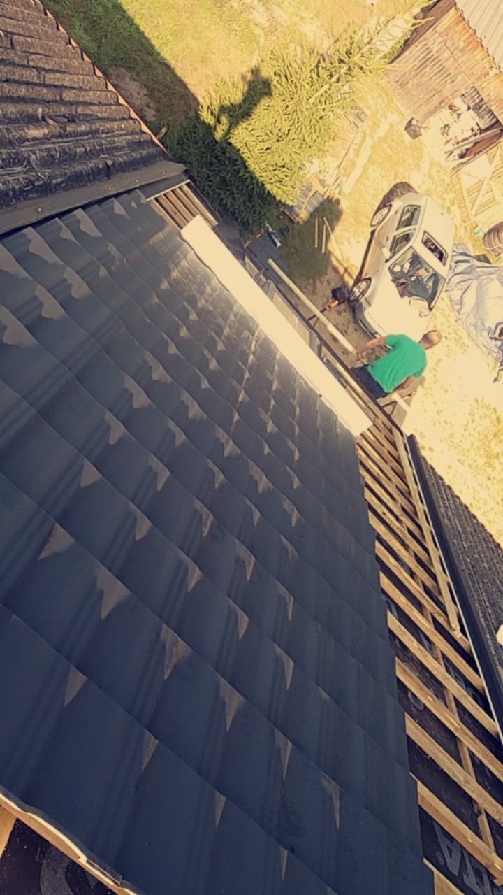 Montaż blachy na dachu domu, widok z góry na pracownika w zielonej koszulce i samochód osobowy