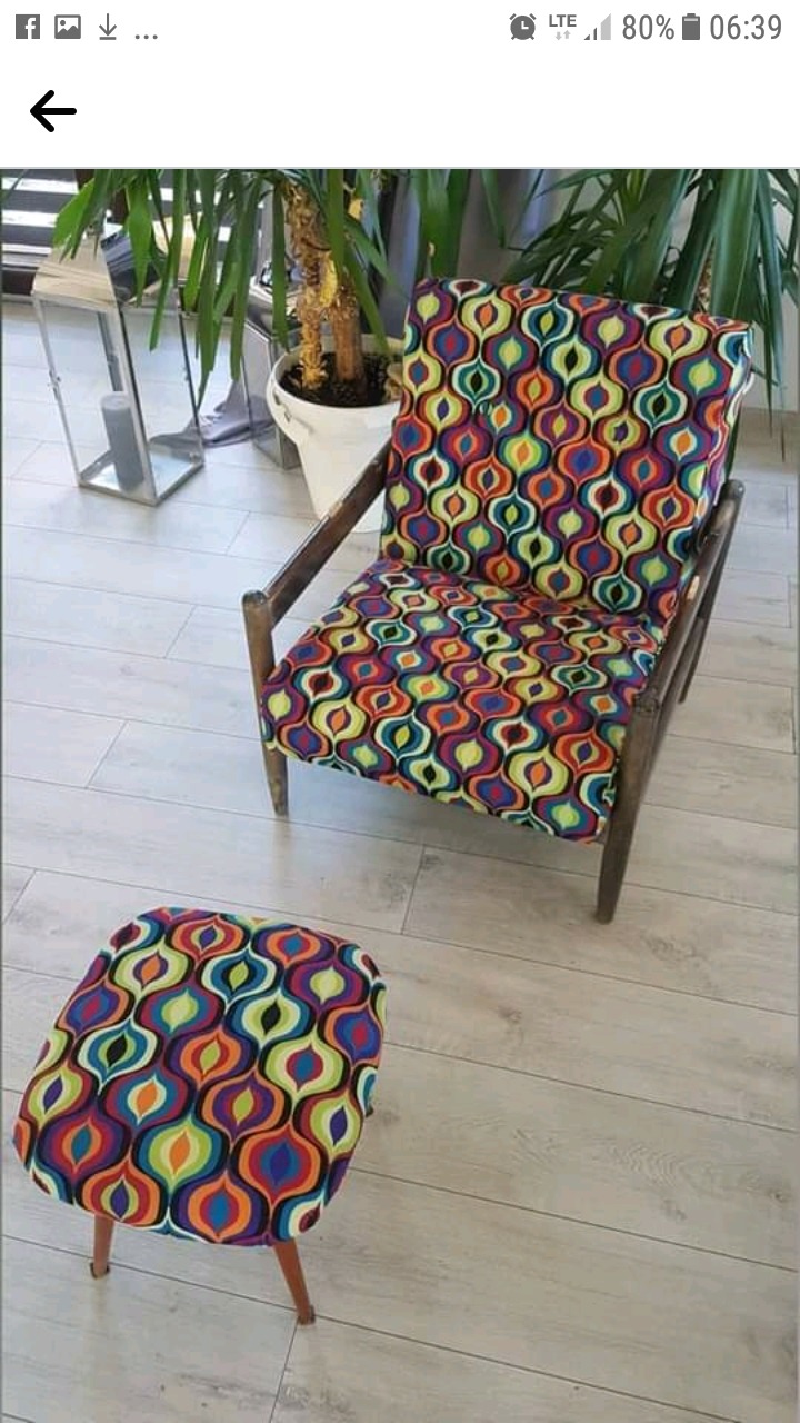 Tapicerowane krzesło i podnóżek w stylu retro, z wzorzystą tkaniną w kolorowe łezki, na tle jasnych paneli podłogowych i rośliny doniczkowej.