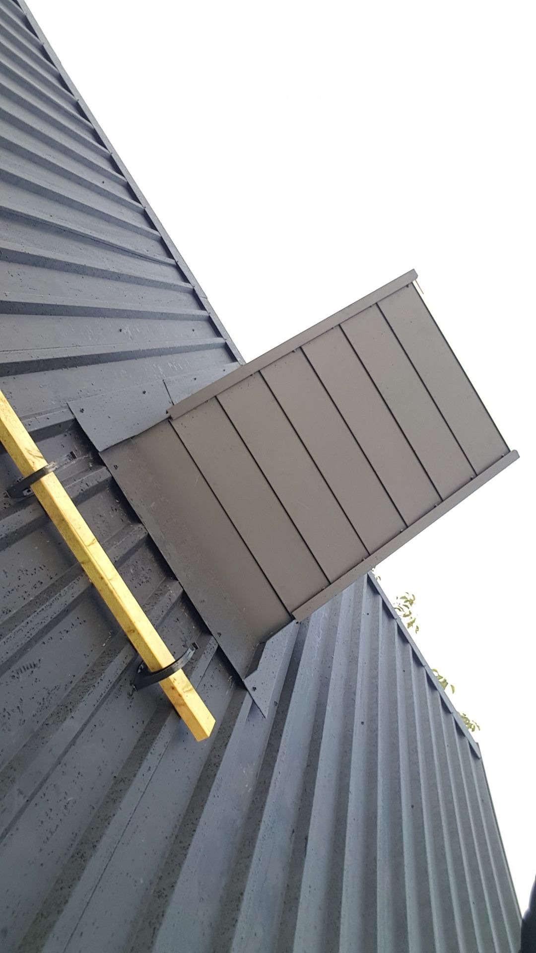 Szary blaszany dach z oknem dachowym w trakcie montażu, widoczna drewniana łata przymocowana do dachu.