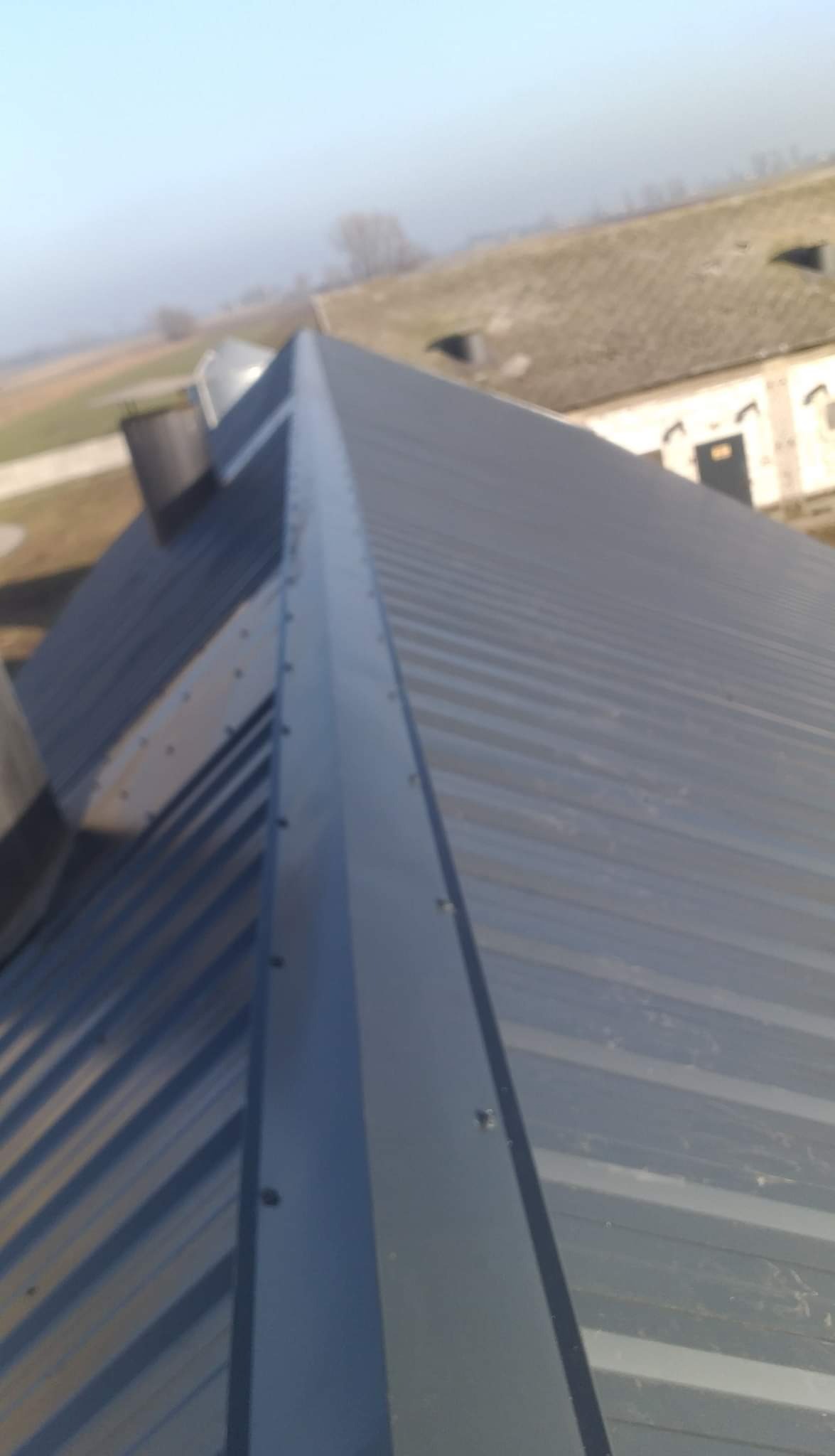 Szary metalowy dach z widocznymi łączeniami na tle rozmytego krajobrazu.