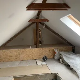 Adaptacja poddasza: widok na ocieploną konstrukcję z płyt OSB, widoczne drewniane elementy więźby dachowej, okno dachowe oraz ślady po pracach wykończeniowych ścian.