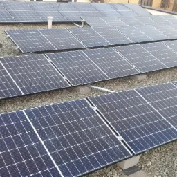 Rząd paneli słonecznych LG zamontowanych na płaskim dachu pokrytym drobnym żwirem, widoczny klimatyzator i komin.