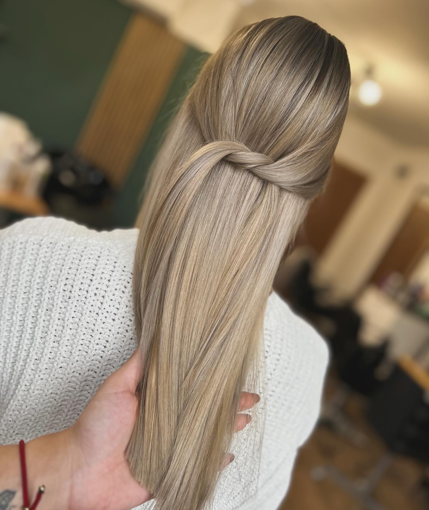 Blond włosy upięte w warkocz z tyłu głowy, widok od tyłu, ręka trzymająca pasmo włosów, sweter z grubym splotem.