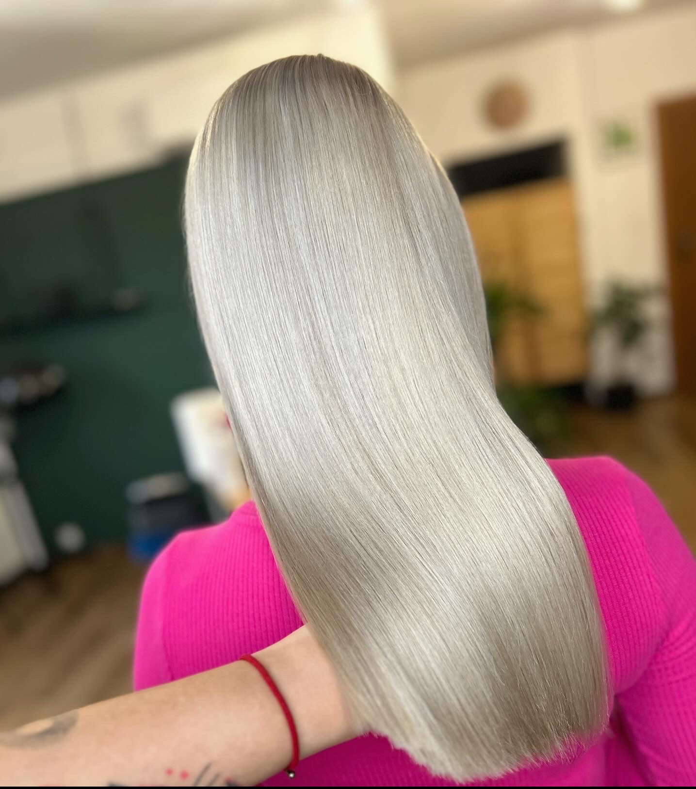 Długie, proste, platynowe włosy z delikatnym cieniowaniem u dołu, widok z tyłu, modelka w różowym swetrze, czerwona bransoletka na nadgarstku.