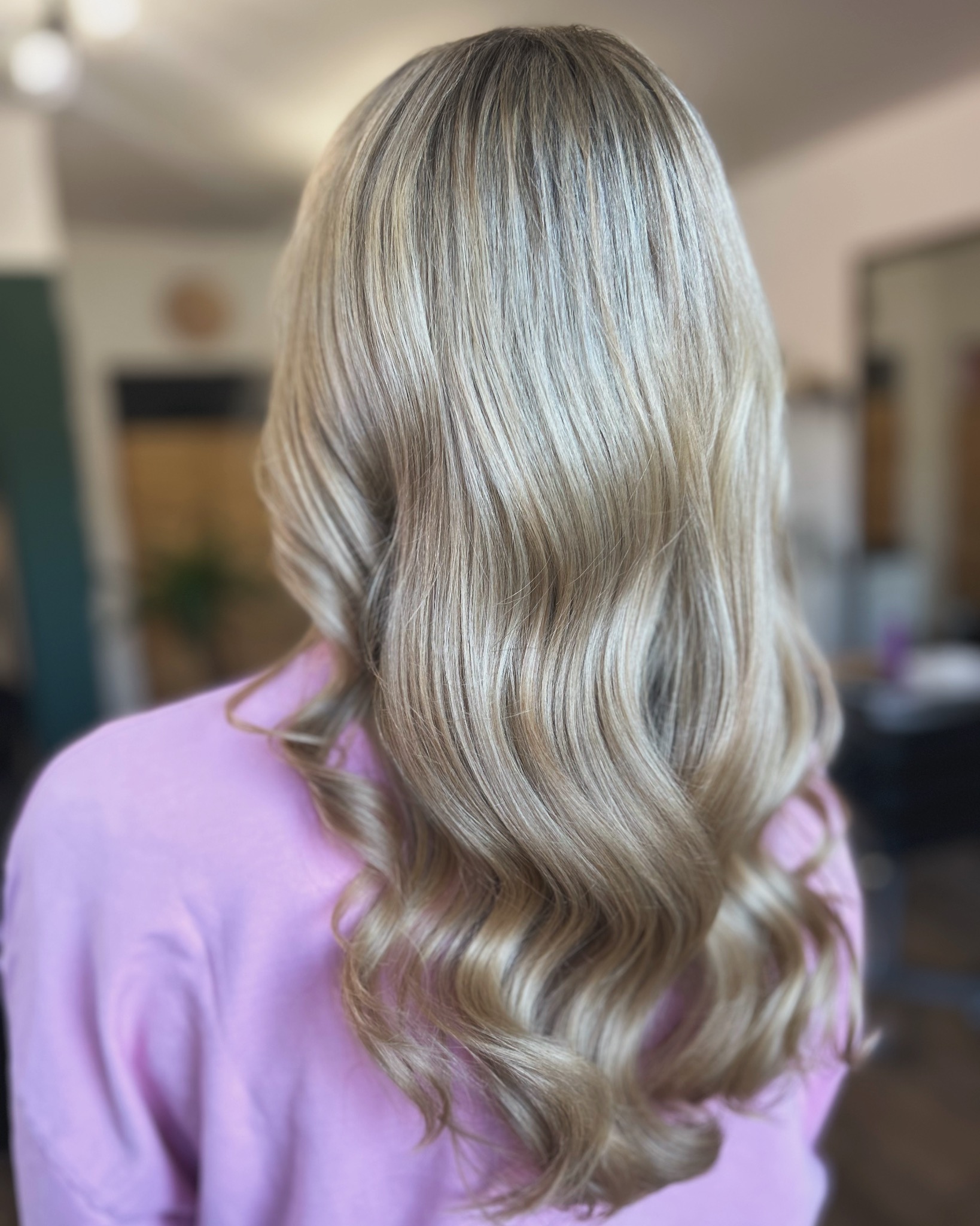 Blond włosy z delikatnymi falami, widoczne od tyłu, wykonane w salonie w Bielsko-Białej, na tle rozmytego wnętrza.