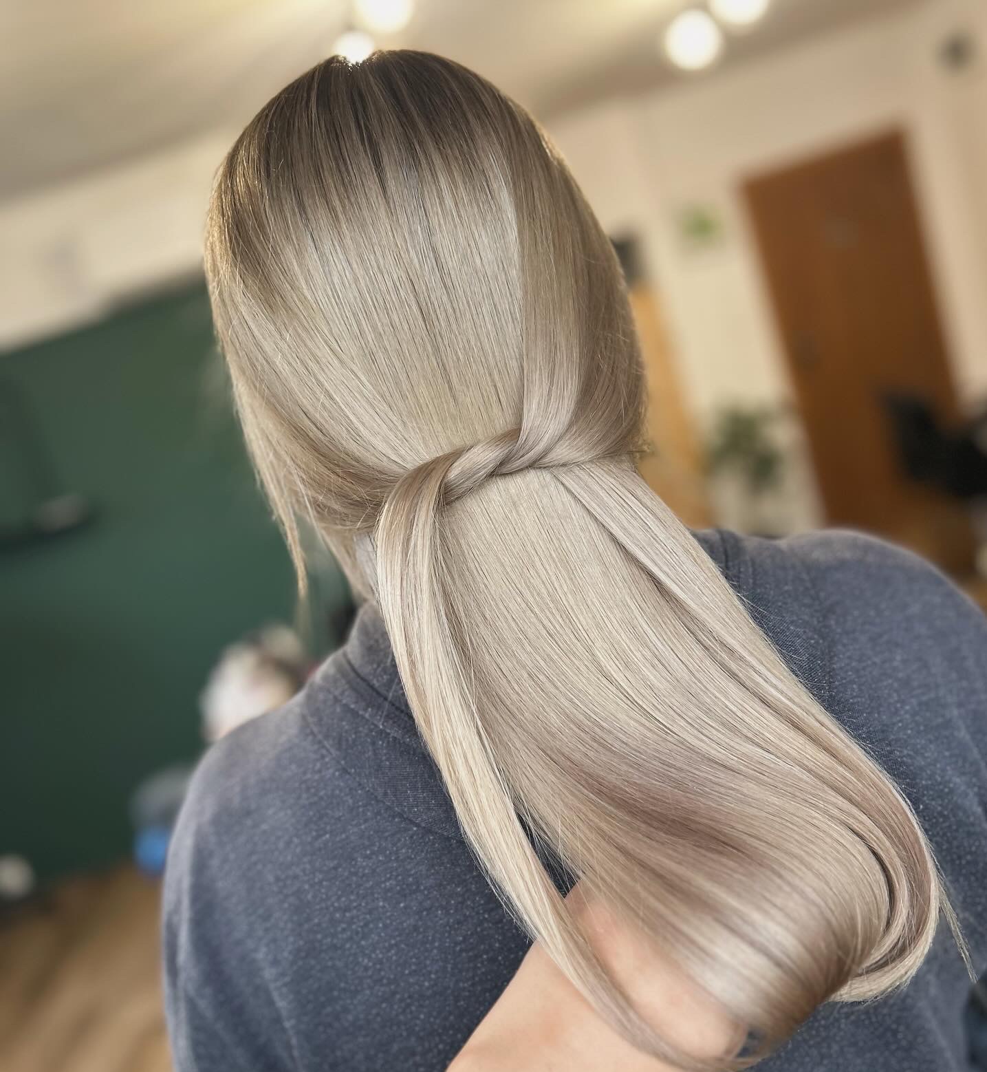 Tył głowy kobiety z długimi, platynowymi włosami związanymi w niski kucyk z owiniętym pasmem, widoczne delikatne cieniowanie koloru.