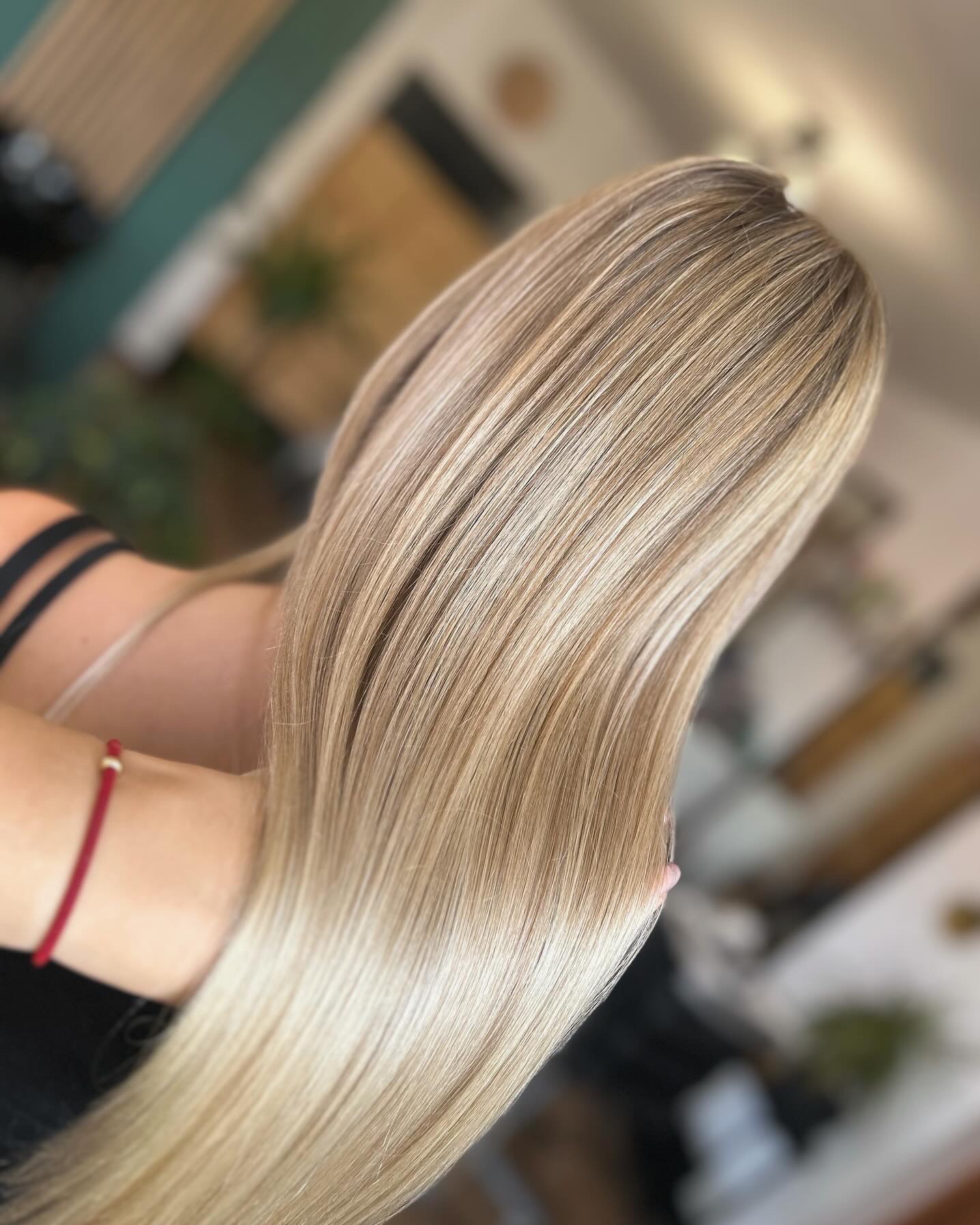 Długie, proste, blond włosy z delikatnymi refleksami, widoczne od tyłu, z czerwonym sznurkiem na nadgarstku