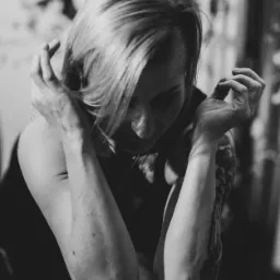 Terapeuta z tatuażami na ramionach, w czerni i bieli, wykonuje głęboki masaż pleców przy użyciu łokci, widoczny fragment kwiatowej dekoracji w tle.