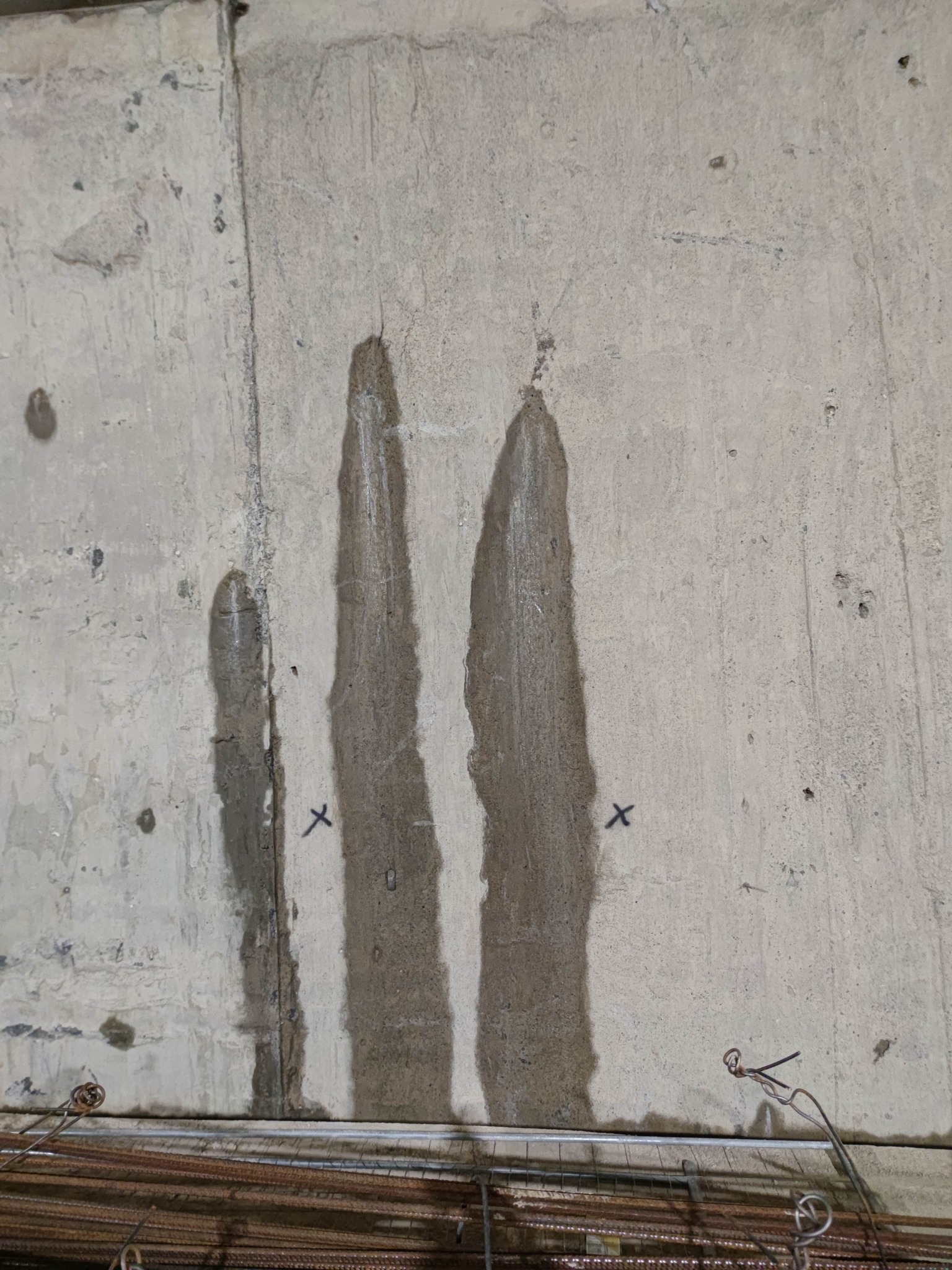 Wilgotna, surowa ściana fundamentowa z widocznymi zaciekami i śladami po montażu szalunków, na dole widoczne pręty zbrojeniowe.