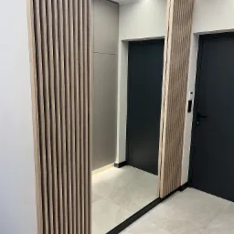 Nowoczesna szafa z lustrem i drewnianymi lamelami w przedpokoju. Minimalistyczny design, neutralna kolorystyka, oświetlenie LED i gładkie, szare drzwi.