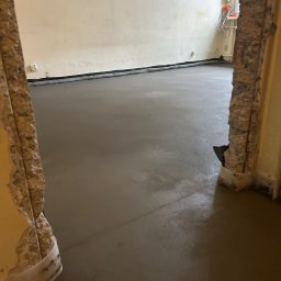 Perfekct Zone Igor Prajwowski - Wylana, świeża wylewka samopoziomująca w pokoju z widocznymi fragmentami zniszczonych ścian i futryny. Widoczne kable elektryczne przy oknie.