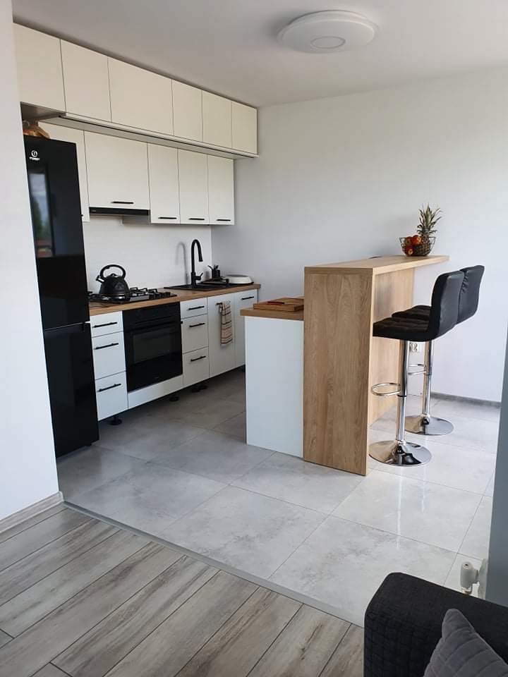 Nowoczesna, jasna kuchnia z białymi szafkami, czarnymi akcentami, blatem z imitacji drewna i barkiem z owocami, sfotografowana z niskiego kąta.