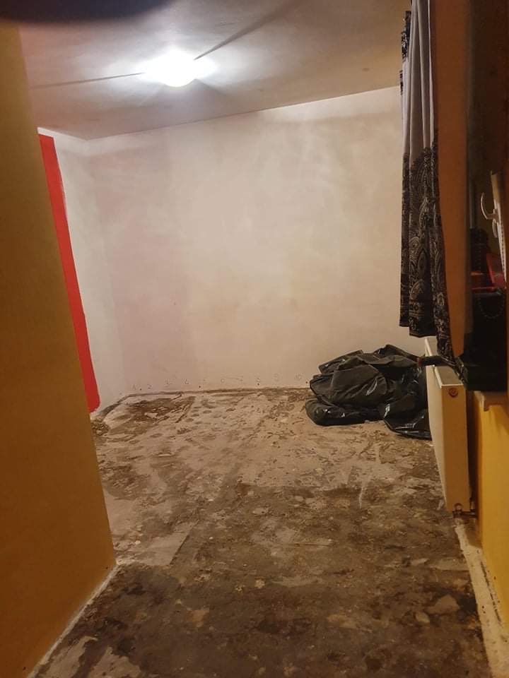 Pokój w trakcie remontu: gołe ściany po szpachlowaniu, podłoga przygotowana do położenia nowej nawierzchni, zakryty grzejnik, widoczne ślady farby na ścianach.