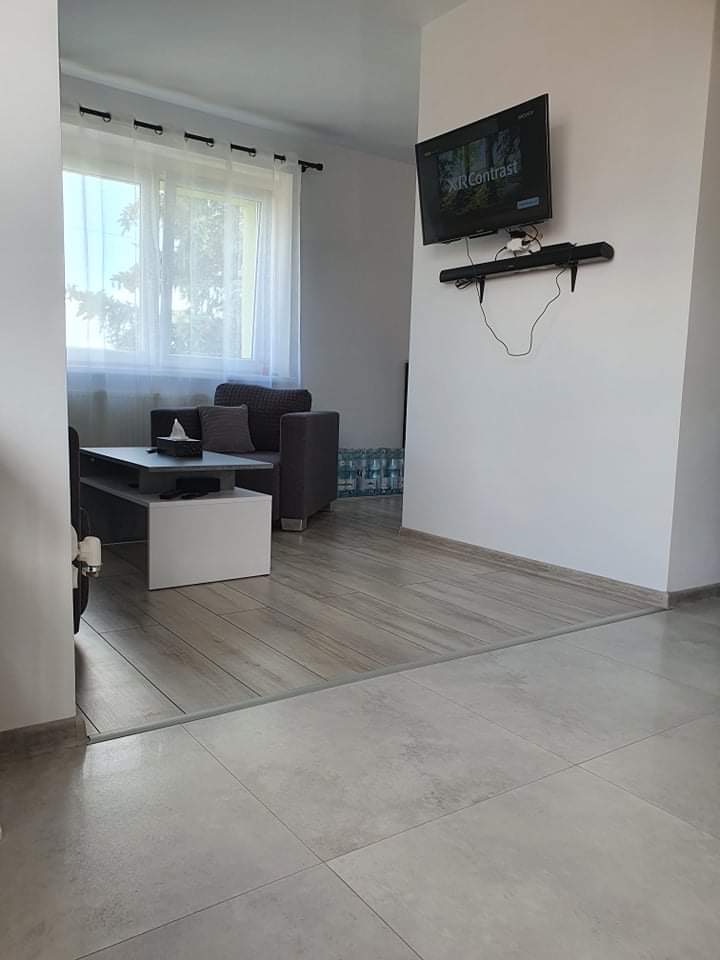 Salon po remoncie z szarą sofą, telewizorem na ścianie i przejściem między dwoma rodzajami podłóg: płytki ceramiczne i panele laminowane.