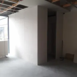 Wnętrze w trakcie prac wykończeniowych: ściany z płyt gipsowo-kartonowych w surowym stanie, widoczna metalowa konstrukcja sufitu i betonowa posadzka.