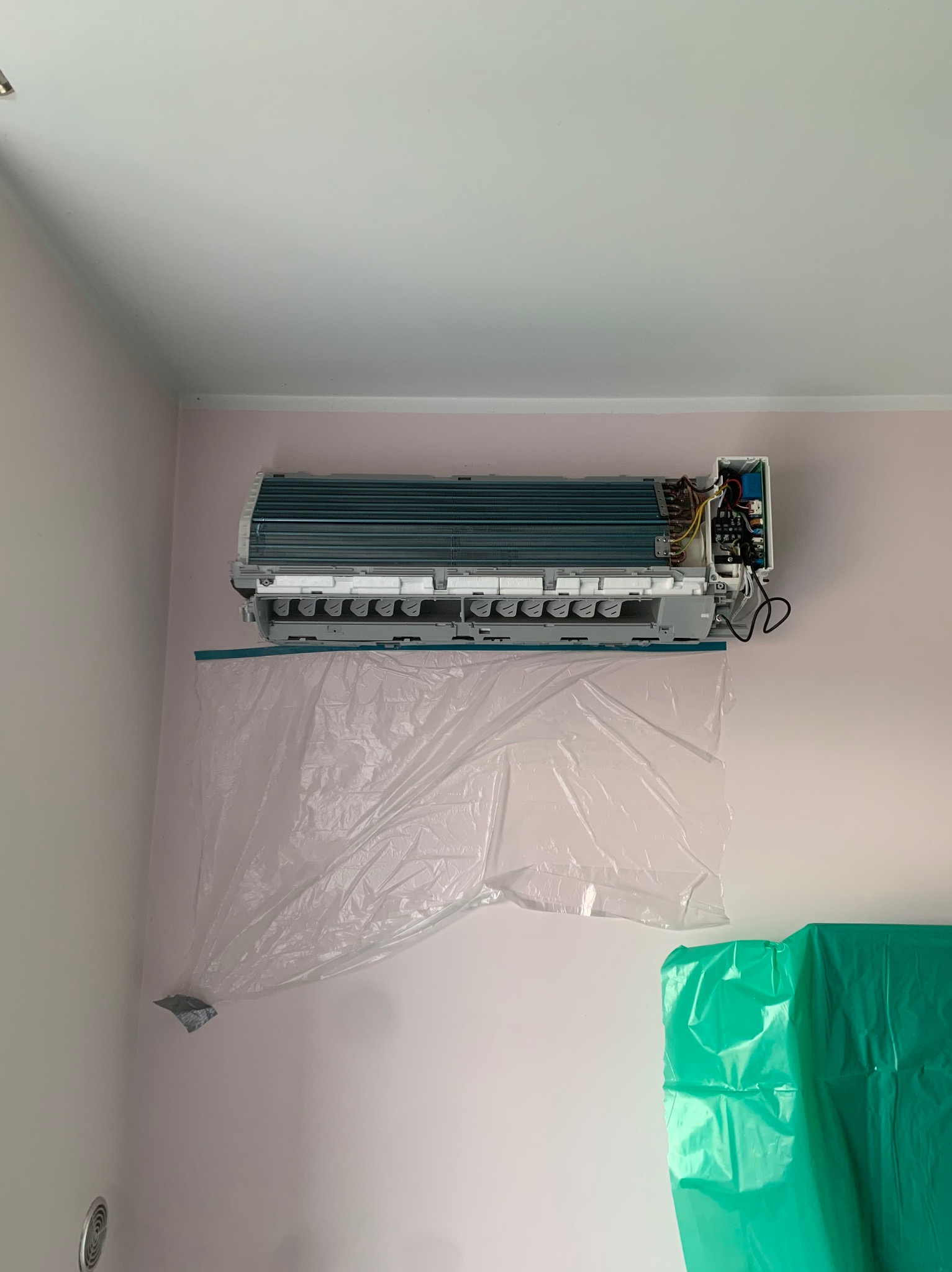 Rozłożony klimatyzator ścienny z otwartą obudową, zabezpieczony folią ochronną podczas serwisu. Widoczne elementy wewnętrzne i przewody.