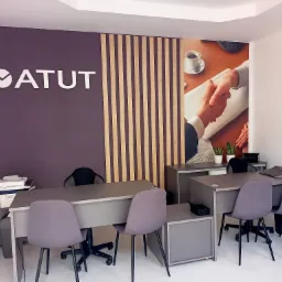 Biuro z logo 'ATUT' na ścianie, drewnianymi lamelami i fototapetą z uściskiem dłoni nad filiżanką kawy. Dwa biurka z szarymi krzesłami i wyposażeniem biurowym.