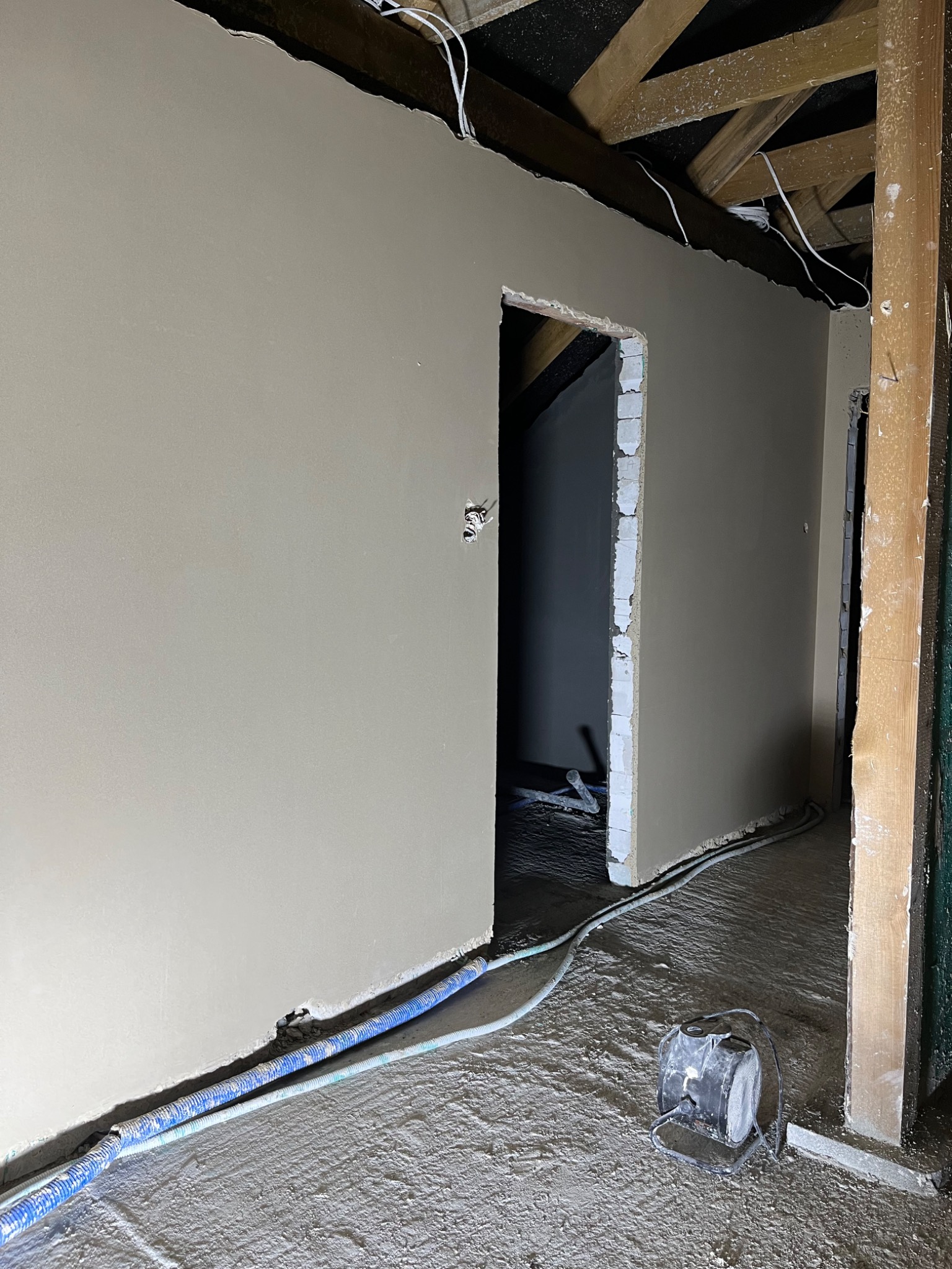 Wnętrze w trakcie prac wykończeniowych, świeżo położona warstwa na ścianach, widoczne przewody elektryczne w korytach i lampa halogenowa na podłodze.