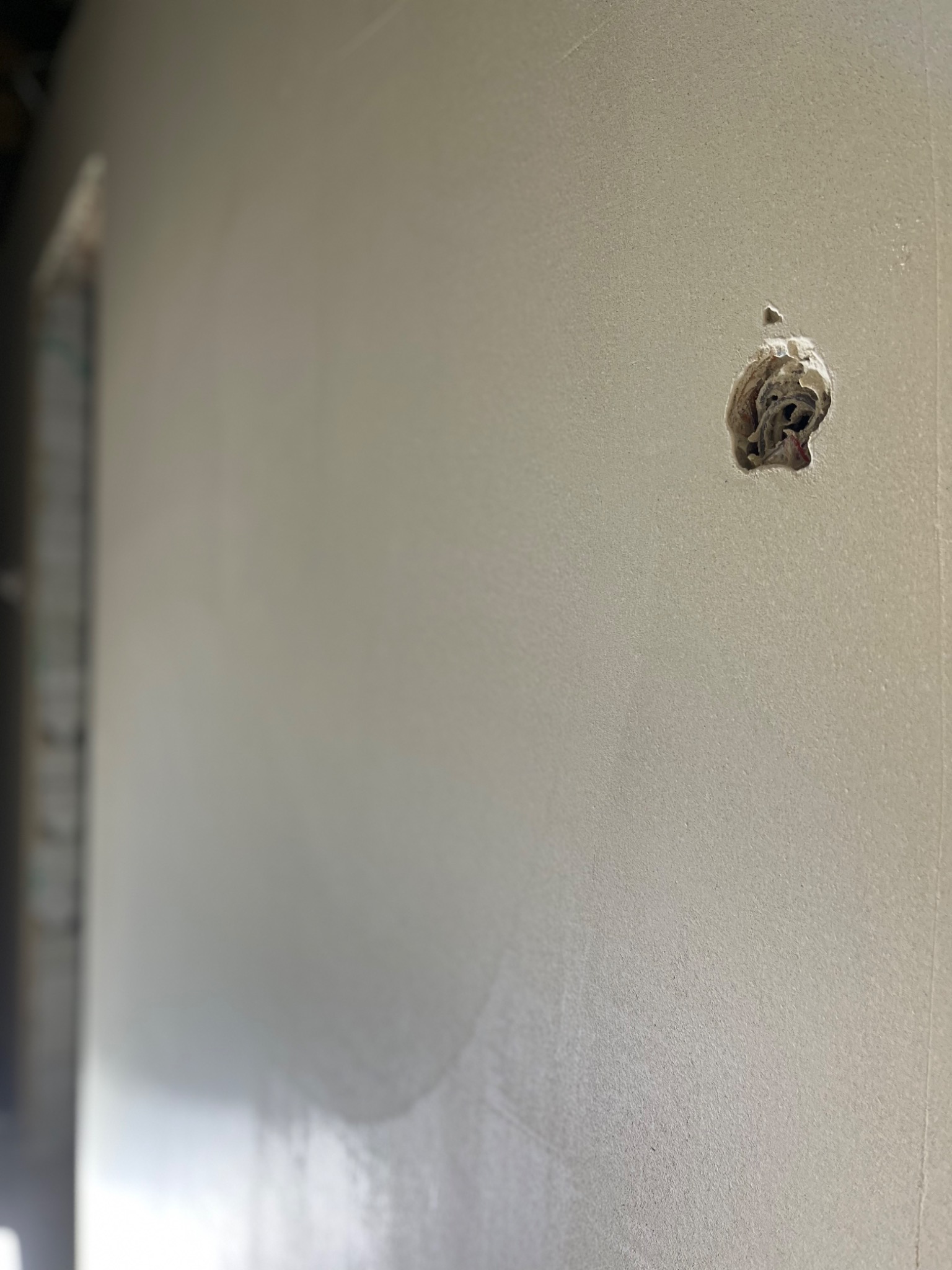 Fragment ściany z widocznym ubytkiem w strukturze, przygotowanym do wypełnienia, z widocznymi fragmentami instalacji wewnątrz.